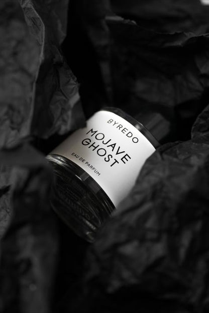 A bottle of Baccarats' "Mojave Ghost EDP for Men and Women." The cylindrical bottle with a transparent body showcases the label proudly displaying the product's name. The round black cap completes its sleek and minimalist appearance, embodying Mojave Ghost as your exotic floral signature scent.