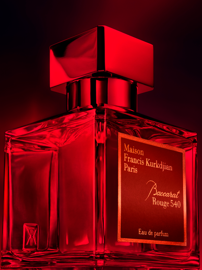 A transparent glass bottle of perfume with a gold cap, featuring "Baccarats Baccarat Rouge 540 Eau de Parfum for Men and Women" in gold and white text on a red background, embodies the essence of an amber floral fragrance.