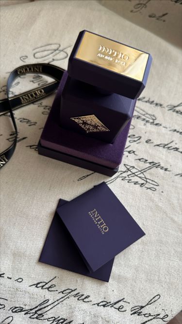 The INITIO SIDE EFFECT EDP 90ml by Baccarats is housed in a dark purple bottle with a square design, featuring a gold embossed decorative emblem at its center. The bottle is topped with a matching square, flat cap and exudes luxury, capturing the essence of rich vanilla and tobacco notes.