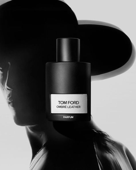 Two black perfume bottles, one labeled "Tom Ford Ombre Leather" and the other "Tom Ford Ombre Leather Parfum 100ml" from Baccarats, are elegantly displayed. Surrounded by dark flowers and wood, these fragrances boast notes of floral leather, black leather, jasmine sambac, cedarwood, and violet leaf.