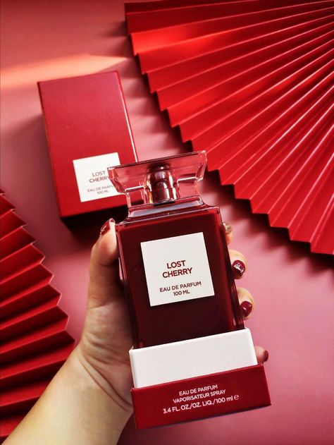 A rectangular, translucent pink bottle with a red liquid inside displays a front label that reads "TOM FORD LOST CHERRY EAU DE PARFUM 100 ML." Infused with the richness of black cherry, the bottle features a square-shaped, translucent pink cap. This unisex fragrance is offered by the brand Baccarats under the name Tom Ford Lost Cherry Eau De Parfum for Men and Women.