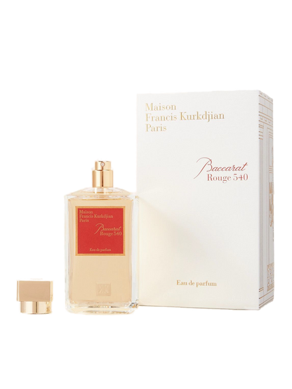 A transparent glass bottle of perfume with a gold cap, featuring "Baccarats Baccarat Rouge 540 Eau de Parfum for Men and Women" in gold and white text on a red background, embodies the essence of an amber floral fragrance.