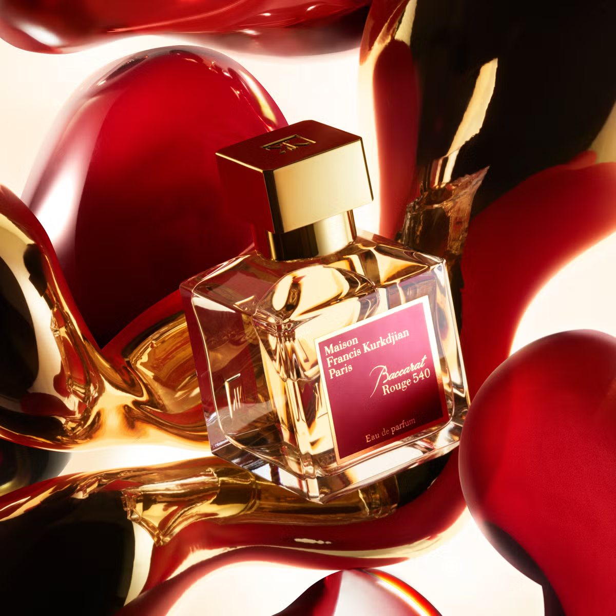 A transparent glass bottle of perfume with a gold cap, featuring "Baccarats Baccarat Rouge 540 Eau de Parfum for Men and Women" in gold and white text on a red background, embodies the essence of an amber floral fragrance.