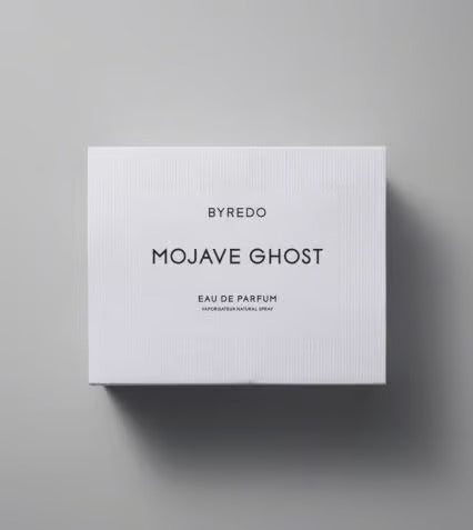 A bottle of Baccarats' "Mojave Ghost EDP for Men and Women." The cylindrical bottle with a transparent body showcases the label proudly displaying the product's name. The round black cap completes its sleek and minimalist appearance, embodying Mojave Ghost as your exotic floral signature scent.