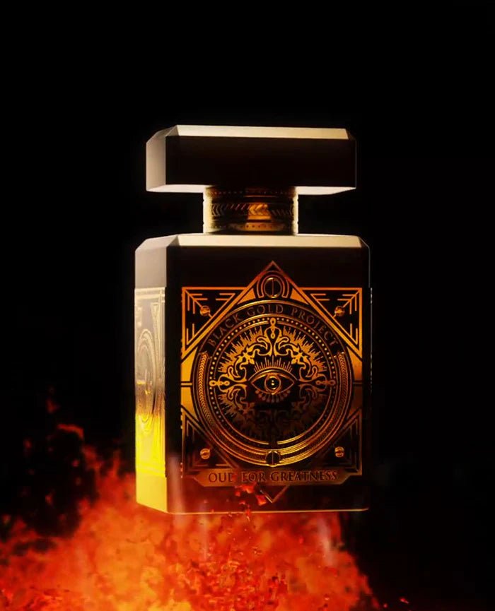 A 90ml bottle of Baccarats' Initio Oud for Greatness EDP. The black bottle, adorned with elaborate gold detailing, features an intricate design highlighted by a prominent eye motif on the front. Infused with rich and captivating notes of patchouli and oud wood, the fragrance exemplifies luxury. The cap is black with elegant gold accents.