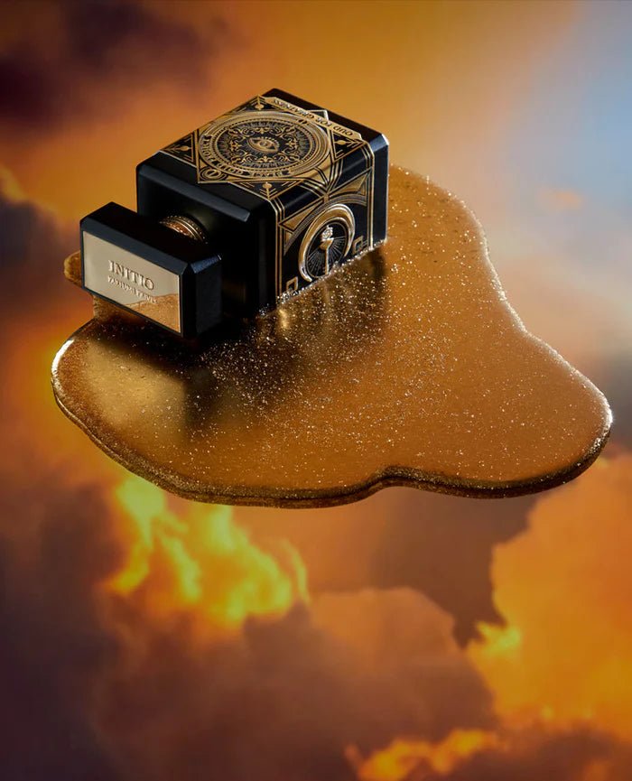 A 90ml bottle of Baccarats' Initio Oud for Greatness EDP. The black bottle, adorned with elaborate gold detailing, features an intricate design highlighted by a prominent eye motif on the front. Infused with rich and captivating notes of patchouli and oud wood, the fragrance exemplifies luxury. The cap is black with elegant gold accents.